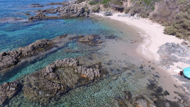 Una playa costera con aguas transparentes, formaciones rocosas y un sendero arenoso.