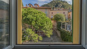 Une vue depuis une fenêtre d’un immeuble, avec une montagne en arrière-plan, un arbre au premier plan et une rue bordée de bâtiments.