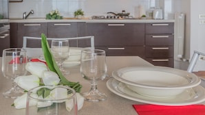 A modern kitchen with dark cabinets, a white countertop, and a dining area set with white plates, glasses, and tulips. - Villa Lisander Varenna (Varenna)