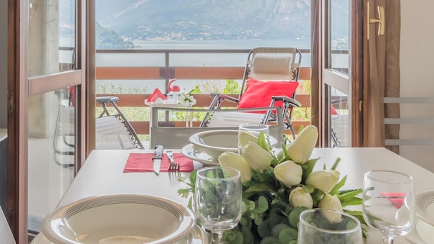 A dining table set with plates, cutlery, and a floral centerpiece, overlooking a mountainous landscape. - Villa Lisander Varenna (Varenna)