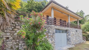 A stone building with a balcony, surrounded by lush greenery and a stone wall. - Villa Lisander Varenna (Varenna)
