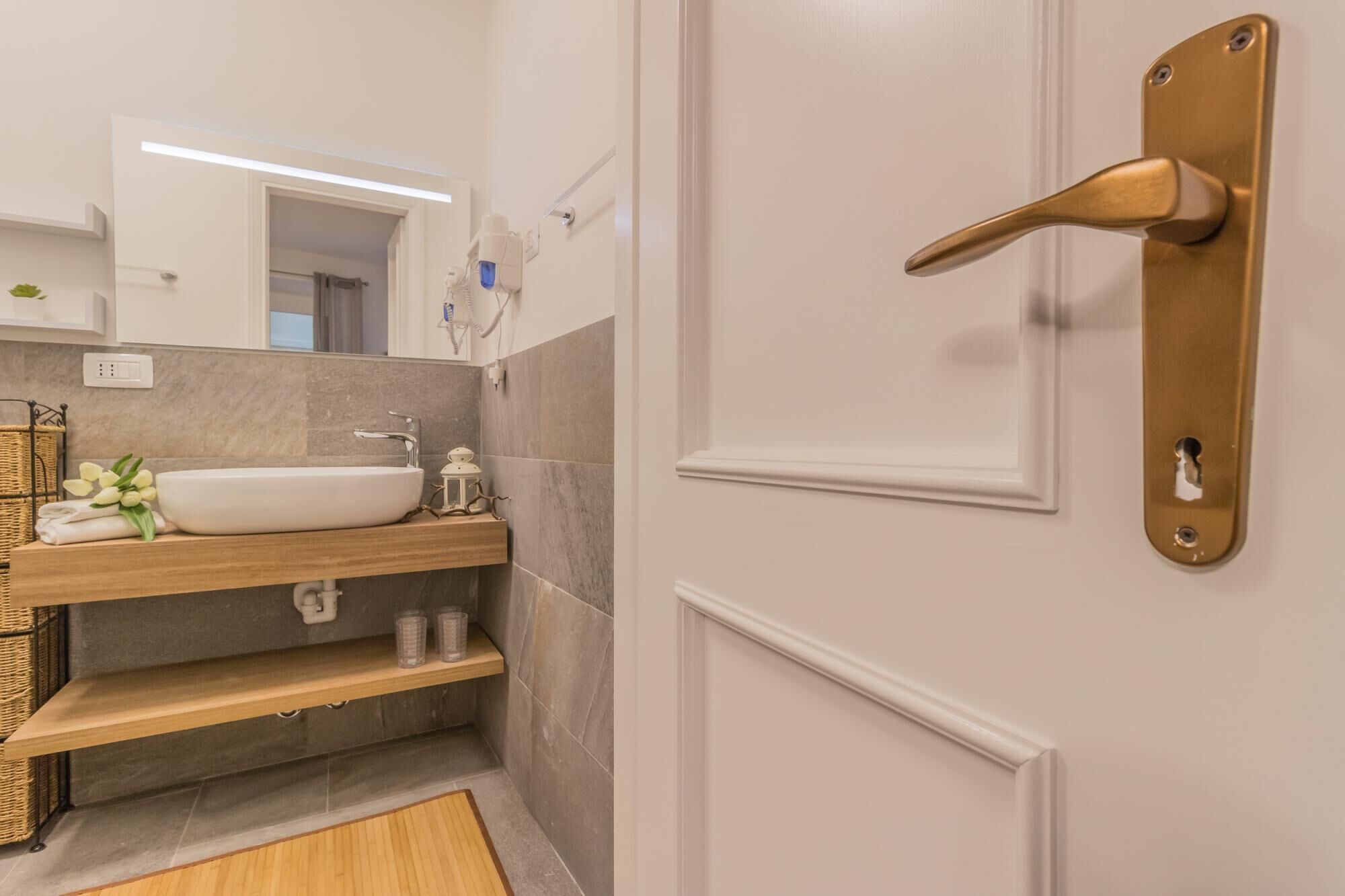 Une salle de bain avec un lavabo blanc, un miroir, un porte-serviettes et une porte dotée d’une poignée en laiton.