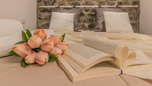 Ein Bett mit weißer Bettwäsche, ein Strauß rosa Blumen und ein offenes Buch auf einer beigen Oberfläche.