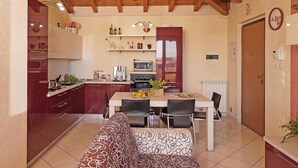 A compact kitchen with a dining area, wooden ceiling beams, and a red door. - Appartamento Tammaro (Sirmione)