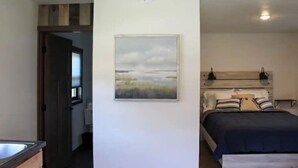 A bedroom with a bed, a nightstand, a wall-mounted lamp, and a painting.