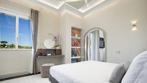 A modern bedroom with a large bed, a vanity with a mirror, and a view of the outdoors. - Villa Nina in Sorrento (Sorrento)