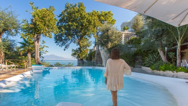 A pool area with a person walking, surrounded by trees and a view of the sea. - Villa Nina in Sorrento (Sorrento)