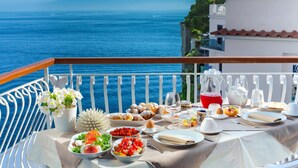 A balcony table set with various dishes and drinks, overlooking a scenic ocean view with a mountain in the distance. - Villa Nina in Sorrento (Sorrento)