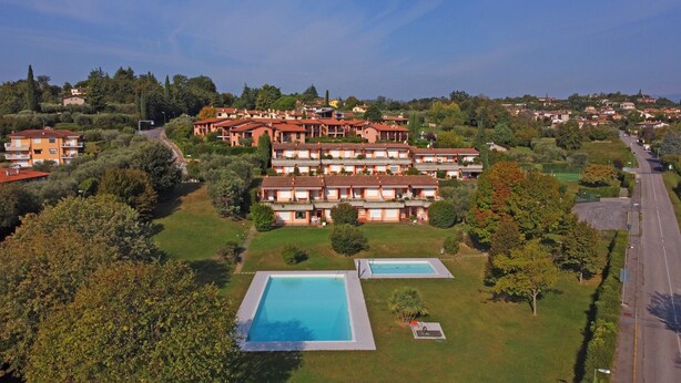 A large hotel with multiple buildings, two swimming pools, and a well-maintained lawn.