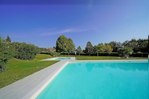 A large outdoor swimming pool with a clear blue water, surrounded by a well-maintained lawn and trees. - Petronella in Soiano (Soiano del Lago)
