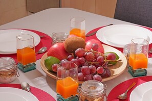 Une table mise pour le petit-déjeuner avec une assiette de fruits, des verres de jus d’orange et un bocal de granola.