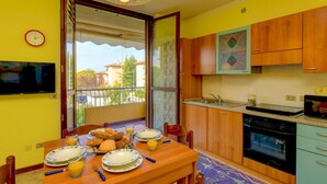 A compact kitchen with wooden cabinets, a built-in oven, and a dining area with a table set for breakfast. - Villaggio dei Fiori - Viola (Sirmione)