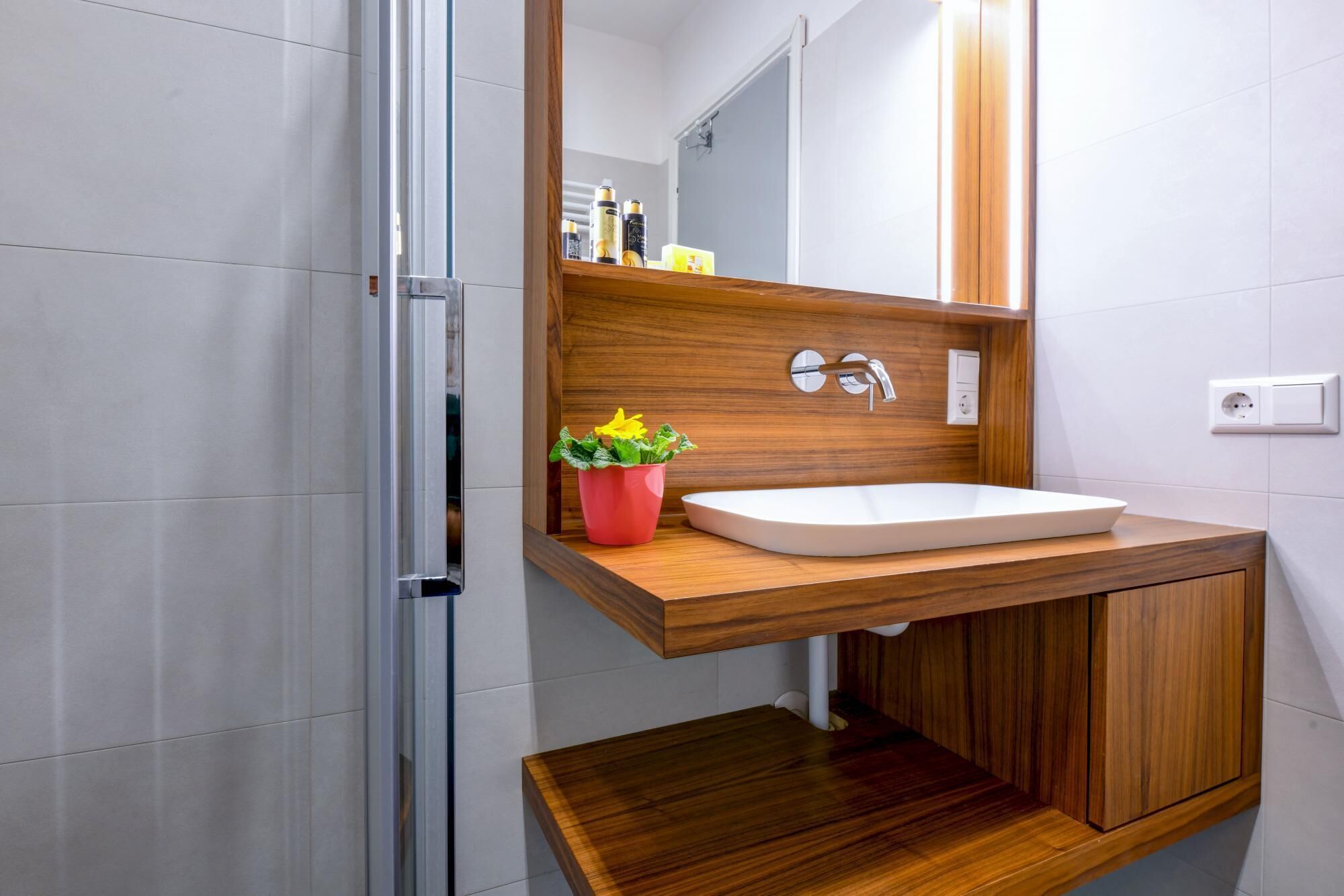 A modern bathroom with a wooden vanity, a white sink, and a mirror above it.