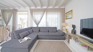 Un salon moderne avec un canapé d’angle gris, un téléviseur à écran plat et une bibliothèque.