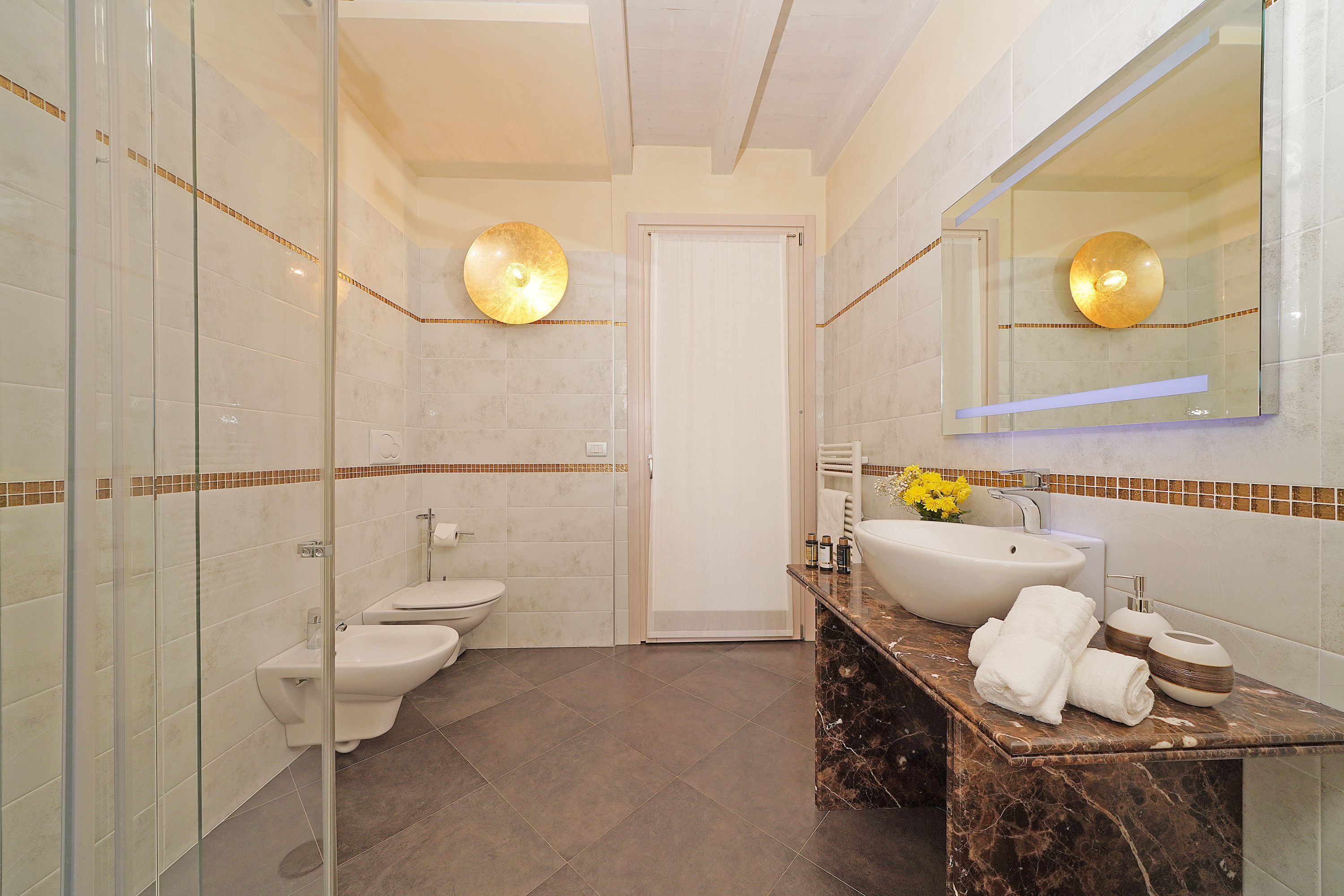 Un baño moderno con cabina de ducha de vidrio, inodoro blanco, lavamanos con encimera de mármol y un espejo grande.