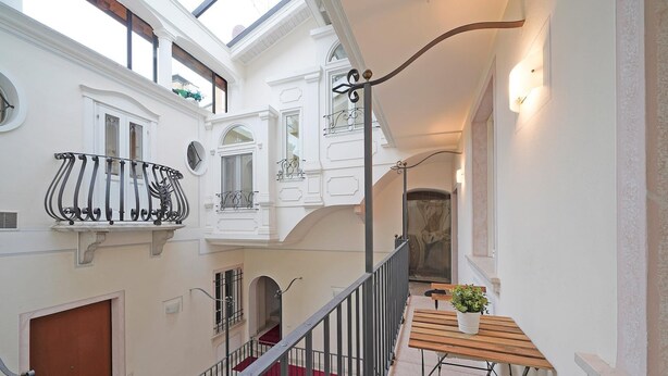 A multi-level interior with a staircase, a wooden bench with a potted plant, and a balcony with decorative iron railings. - Downtown Apartment in Sal (Salò)