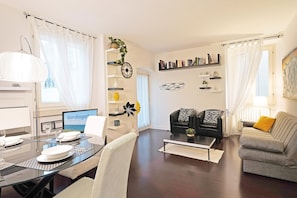 A modern living room with a dining area, featuring a glass table, a sofa, a coffee table, and a bookshelf. - Downtown Apartment in Sal (Salò)