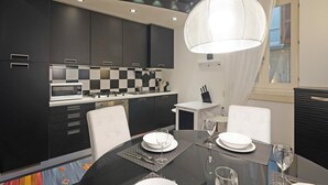A modern kitchen with dark cabinetry, a checkered backsplash, and a dining area with a glass table set for two. - Downtown Apartment in Sal (Salò)