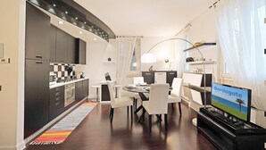 A modern kitchen with dark cabinets and a dining area with a round table and white chairs. There is a television on a stand with a view of the sea. - Downtown Apartment in Sal (Salò)