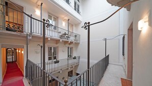 A multi-level interior with a red carpeted staircase, balconies with potted plants, and a white wall with a light fixture. - Downtown Apartment in Sal (Salò)
