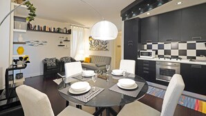 A modern kitchen with dark cabinets, a microwave, and a gas stove. There is a dining area with a round table set for four, and a sofa in the background. - Downtown Apartment in Sal (Salò)