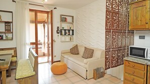 A cozy living room with a sofa, ottoman, and wooden furniture. A bookshelf and decorative wall paneling are visible. - Appartamento Balander (Sirmione)