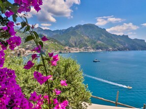 A coastal view with mountains, a boat, and vibrant flowers. - Villa With Terrace and sea View in Ravello ID 3196 (Ravello)