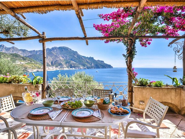 Enjoy a meal under the shade of a pergola with a scenic view of the sea and distant mountains.