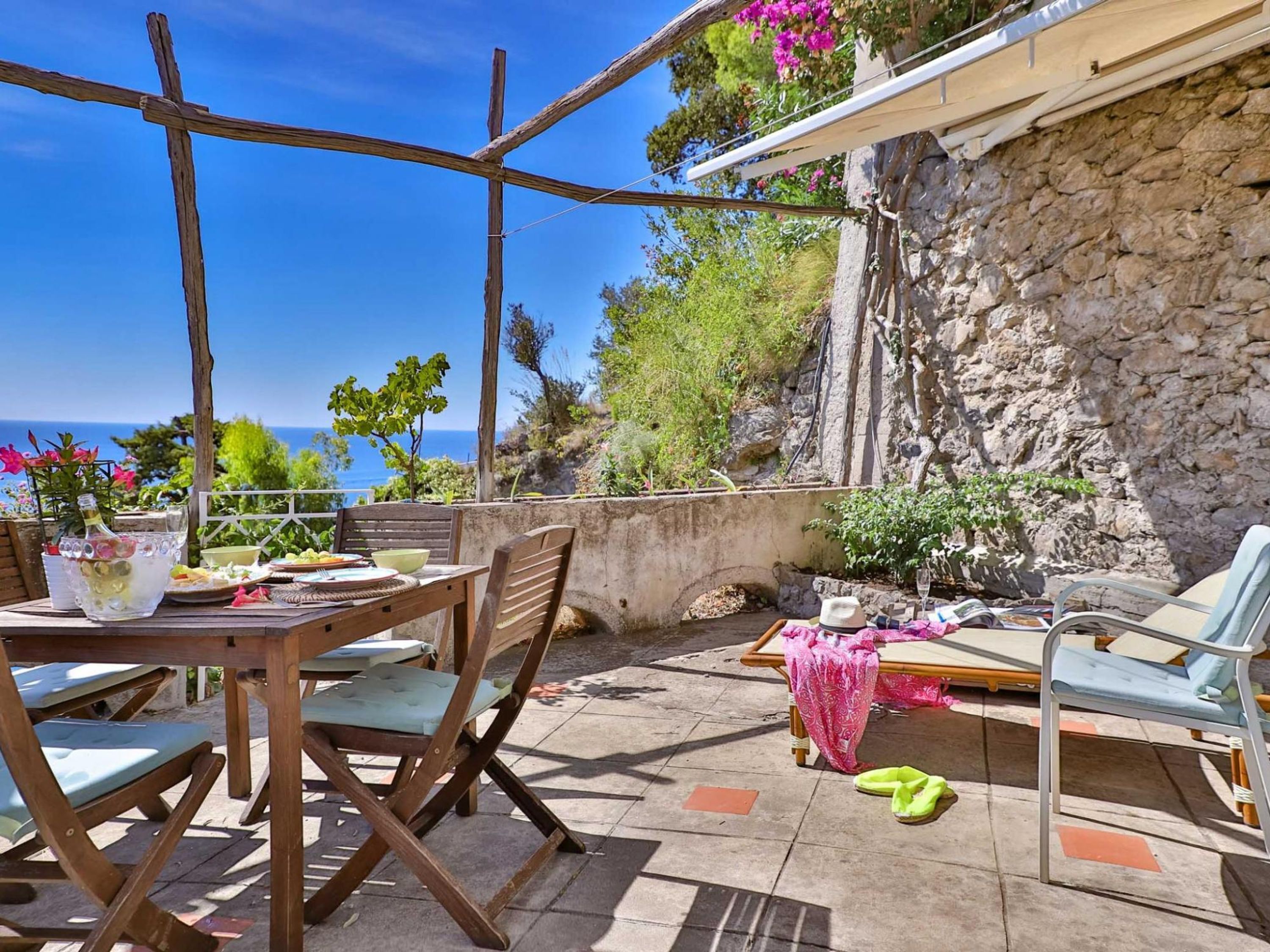 Une terrasse avec une table dressée pour le repas, des chaises et une vue sur la mer.