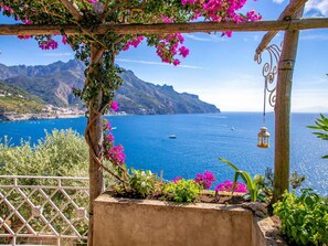 Relax amidst lush green hills and a serene coastal scene, with a picturesque pergola and clear blue sea views.