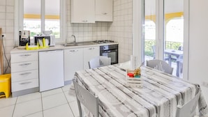 A compact kitchen with white cabinets, a gas stove, and a sink. There is a dining area with a table and chairs, and a view of the outdoors through a sliding glass door.