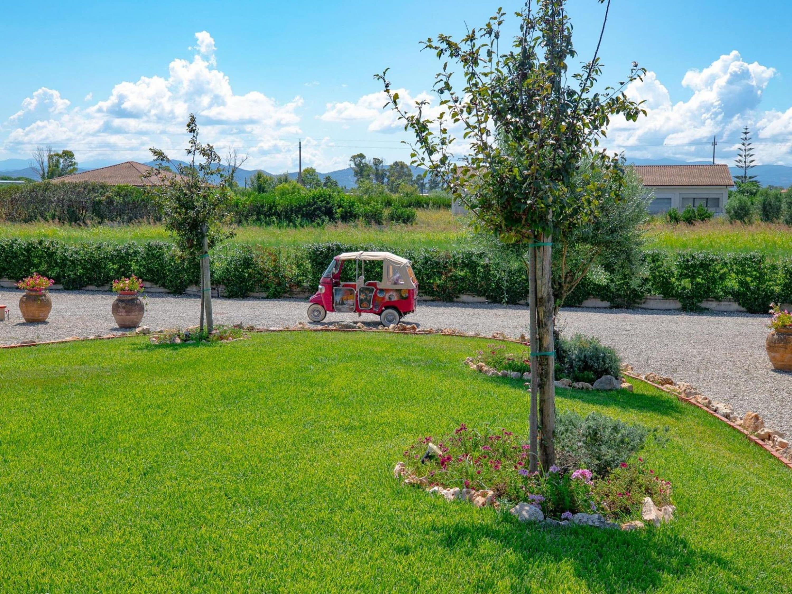 Un vehículo rojo estacionado en un jardín cuidado con cielo despejado.