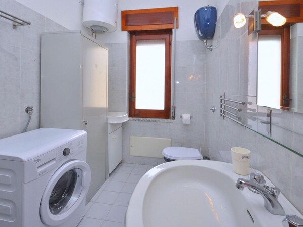 Ein kleines Badezimmer mit Waschmaschine, Toilette, Waschbecken und Spiegel.