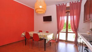 Ein Essbereich mit Tisch und Stühlen, einem Fernseher an der Wand und einer Küchenzeile mit Spüle und Schränken.