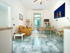 Ein Wohnzimmer mit einer Couch, einem Esstisch mit Stühlen, einem kleinen Tisch mit einer Vase und einem Gemälde an der Wand.