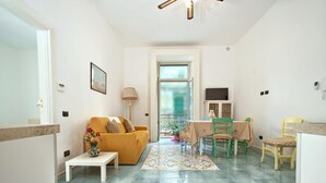 A living room with a sofa, a dining table with chairs, a small table with a vase, and a window with a view. - Appartamento a Vietri sul Mare ID 3050 (Vietri sul Mare)