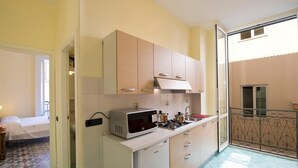 Cozinha compacta com micro-ondas, fogão e armários, que dá para uma varanda com grade de metal.