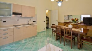 A kitchen with cabinets, a sink, a dining table with chairs, a chandelier, and a television. - Appartamento a Vietri sul Mare ID 3055 (Vietri sul Mare)