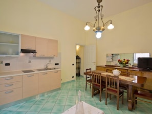 A kitchen with cabinets, a sink, a dining table with chairs, a chandelier, and a television.