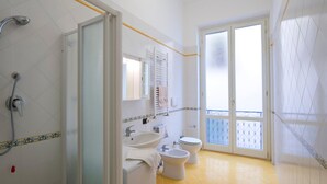A bathroom with a shower, sink, and toilet, a balcony with a view, and a door leading to another room. - Appartamento a Vietri sul Mare ID 3055 (Vietri sul Mare)