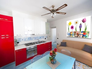 A kitchen with red cabinets, a white countertop, and a dining area with a blue table.