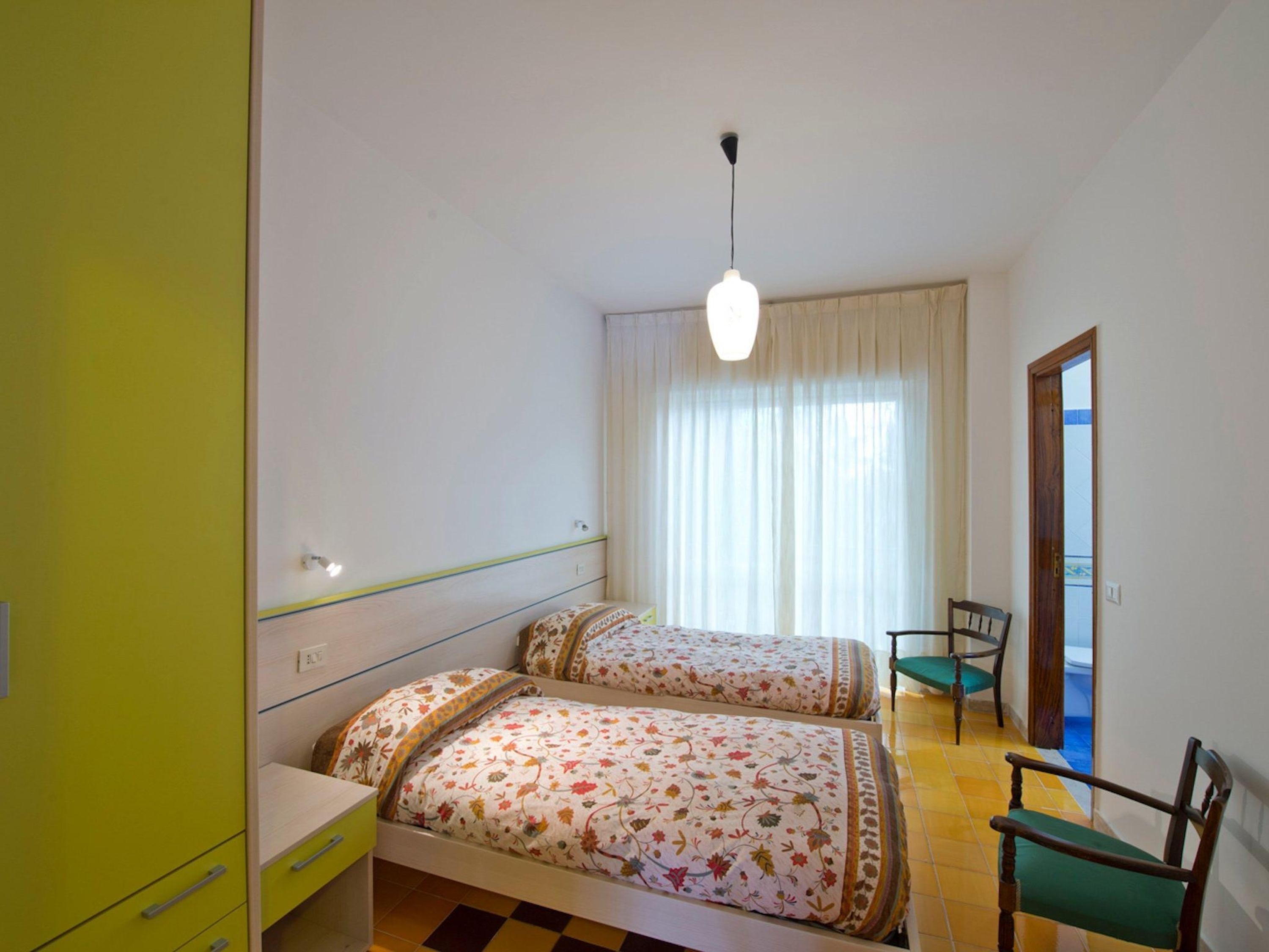 Une chambre avec deux lits, une chaise, un bureau et une fenêtre avec des rideaux.