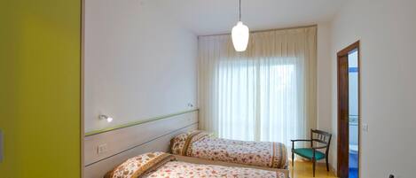 Une chambre avec deux lits, une chaise, un bureau et une fenêtre avec des rideaux.