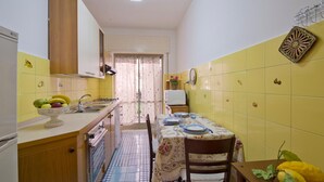 Une cuisine compacte avec un coin repas, comprenant un plan de travail carrelé, un évier, une cuisinière et une table à manger dressée avec des assiettes et un saladier de fruits.
