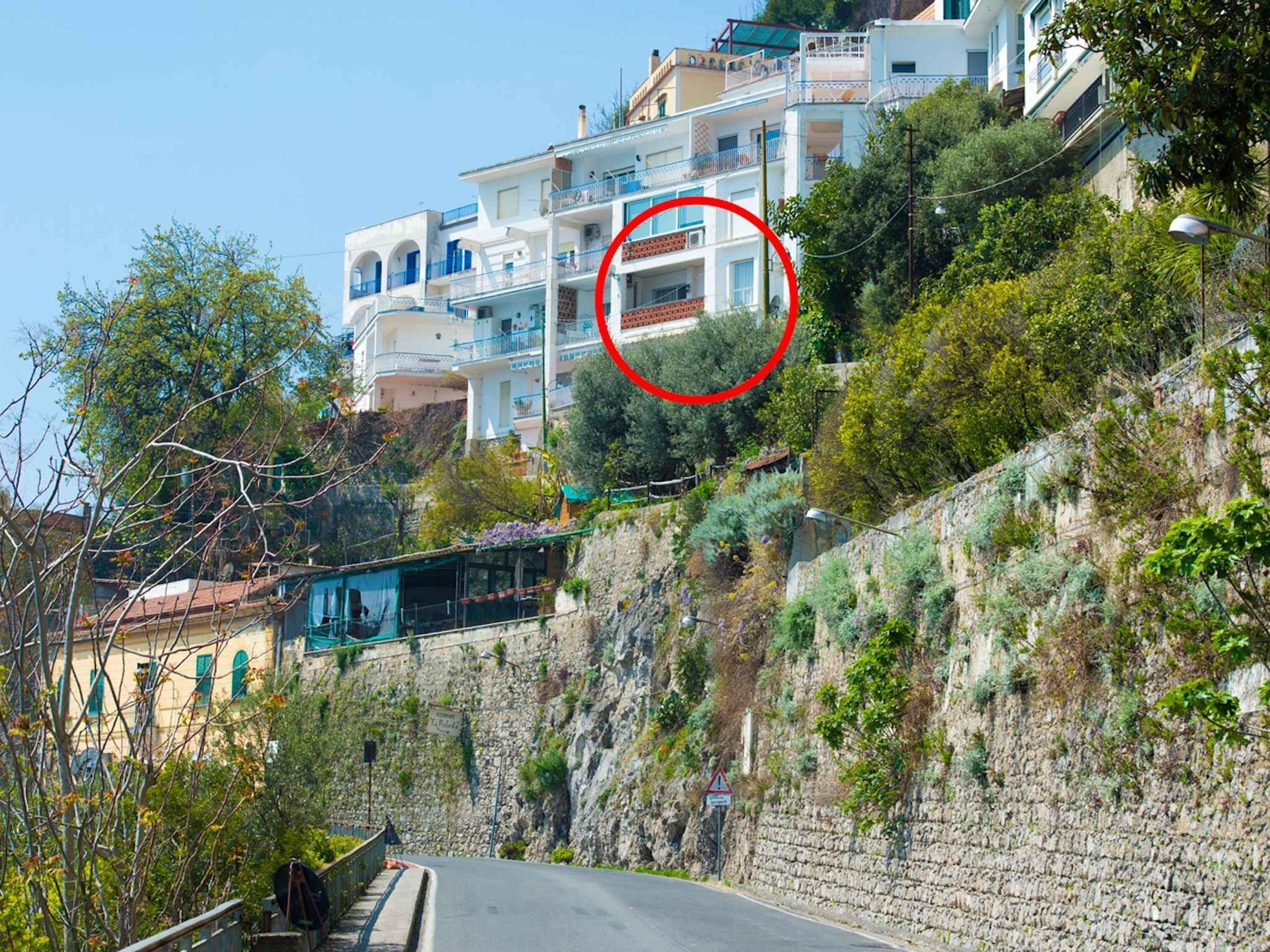 Un barrio residencial en una ladera con edificios de varios pisos, un muro de piedra y una carretera que desciende.