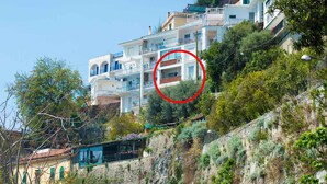 Un quartier résidentiel situé sur une colline, avec des immeubles à plusieurs étages, un mur de soutènement en pierre et une route qui descend en virage.