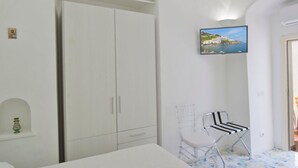 Une chambre à coucher comprenant un lit, une armoire, une chaise et un tableau représentant un paysage côtier.