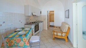 Cozinha compacta com armários brancos, uma mesa de jantar posta com pratos e copos, e uma cadeira de madeira.