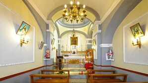 Interior de igreja com bancos de madeira, altar central e arte religiosa nas paredes.
