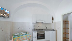 Cozinha compacta com armários brancos, fogão a gás e forno embutido. Há uma mesa de jantar com cadeiras e toalha de mesa colorida.